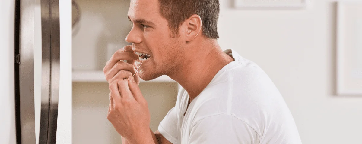 Do I Really Need to Floss? - man flossing his teeth in front of a mirror